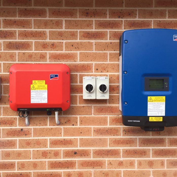 Red and Blue SMA inverters attached to a brick wall