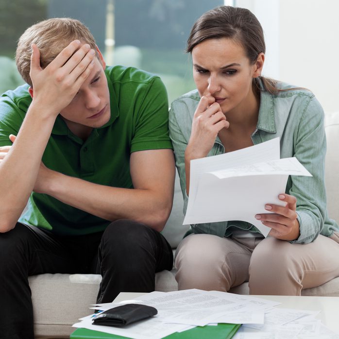Worried young couple sitting on sofa and checking the bills